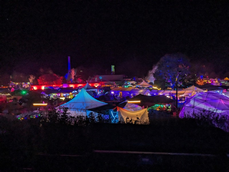 Blick über einige Zelte bei Nacht, alles ist bunt beleuchtet. Am rechten Rand unsere geodätische Kuppel.